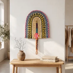 A colorful woven palm leaf fan hung as wall decor above a light wood console table in a bright boutique.