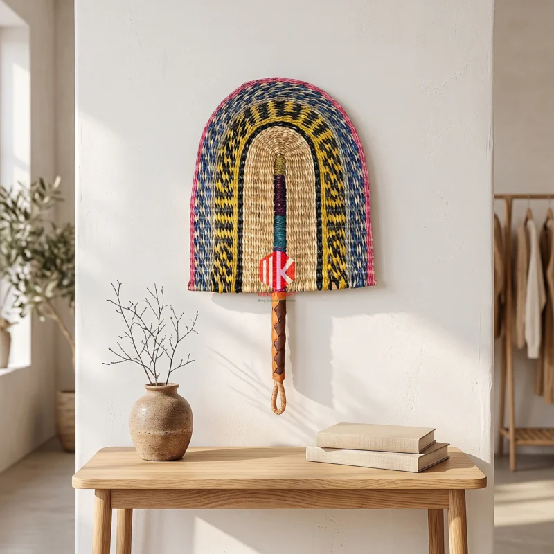 Multicolor Twill Woven Palm Leaf Hand Fan 5 A colorful woven palm leaf fan hung as wall decor above a light wood console table in a bright boutique.