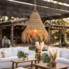 Chevron Woven Palm Leaf Conical Lampshade with Raw Fringe 2 A conical palm leaf lampshade with a shaggy fringe hanging from a wooden beam in a sunlit outdoor wedding lounge.