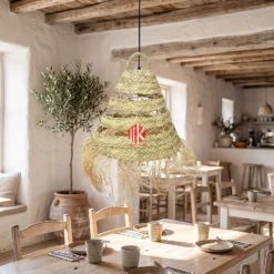 A handwoven palm leaf lampshade hanging over a wooden dining table in a sunlit coastal villa.