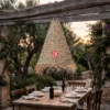 A conical palm leaf lampshade with a fringed edge hangs from a tree branch at an outdoor evening wedding.