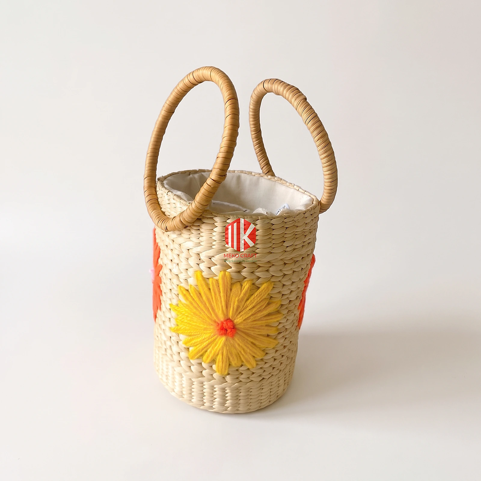Floral Embroidered Seagrass Round Handbag with Circular Handles 3 A studio shot of a cylindrical seagrass handbag with yellow floral embroidery and circular handles on a pure white background.