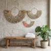Handwoven Palm Leaf Fan Wall Decor Set of 3 2 A set of three palm leaf fan wall decors hung in a staggered arrangement on a white plaster wall in a luxury spa lounge.