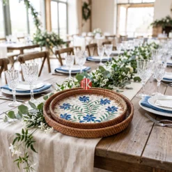 A pair of round trays with blue floral mother of pearl mosaic centers resting on a white table next to a flower.