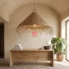 A fringed palm leaf lampshade hanging over a wooden dining table in a sunlit coastal resort.