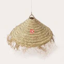 Close-up of a conical braided palm leaf lampshade with a natural fringed rim on a white background.