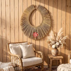 A handwoven palm leaf oval mirror frame with a long shaggy fringe hanging on a white wall in a boho-style event lounge.