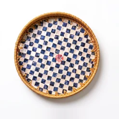 Overhead studio shot of a round serving tray with a woven rattan rim and a checkerboard pattern of white mother of pearl and blue squares on a white background.