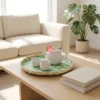 A round bamboo tray with a green geometric pattern sits on a light oak coffee table holding a white ceramic teapot and two cups.
