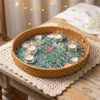 Rattan and Mother of Pearl Round Serving Tray 1 A round mixed material serving tray with a mother of pearl base sits on a rustic wooden table, holding small glass votives and scattered rose petals for an elegant event.