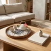 Round mother of pearl serving tray with black pinwheel mosaic and rattan rim resting on a wooden coffee table beside ceramic tea cups