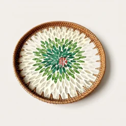 Round mother of pearl tray featuring a green floral shell mosaic center and woven natural rattan rim on a pure white background.