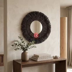 A dark brown fringed seagrass mirror hanging on a light grey plaster wall above a minimalist wooden console table in a luxury spa.