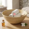 A round spun bamboo bowl containing several rolled white cotton towels on a marble counter in a luxury spa.