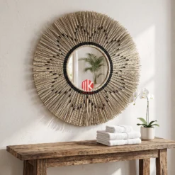 A sunburst palm leaf mirror hung on a soft beige wall in a luxury spa lounge, reflecting a potted palm tree.