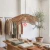 Wavy Rim Seagrass Pendant Lampshade 1 A wavy seagrass lampshade hanging over a minimalist wooden display table in a brightly lit boutique store.