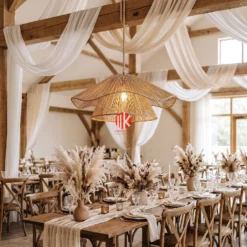 A handwoven wavy seagrass lampshade hanging over a rustic wooden dining table in a boho wedding reception.